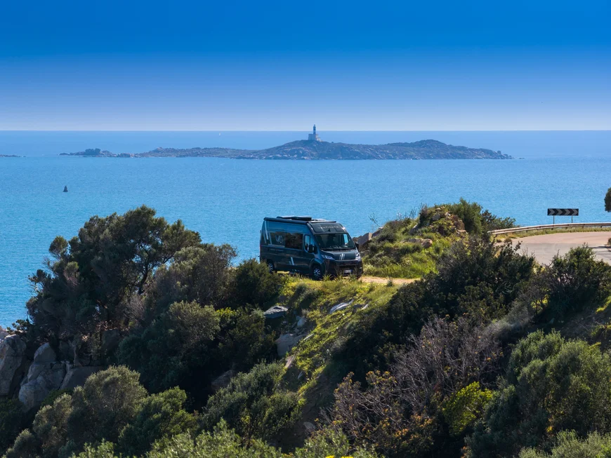 Scopri la Sardegna in van Camper parcheggiato su una scogliera con vista mare e faro sull'isola lontana