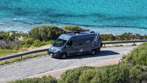 Scopri la Sardegna in van Camper parcheggiato su una strada vicino al mare turchese e vegetazione verde