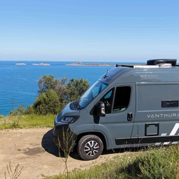 Scopri la Sardegna in van Camper grigio parcheggiato su strada sterrata vicino al mare con isole sullo sfondo