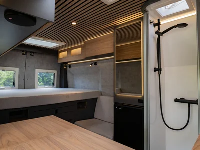 Scopri la Sardegna in van Interno moderno di camper con letto, tavolo e doccia